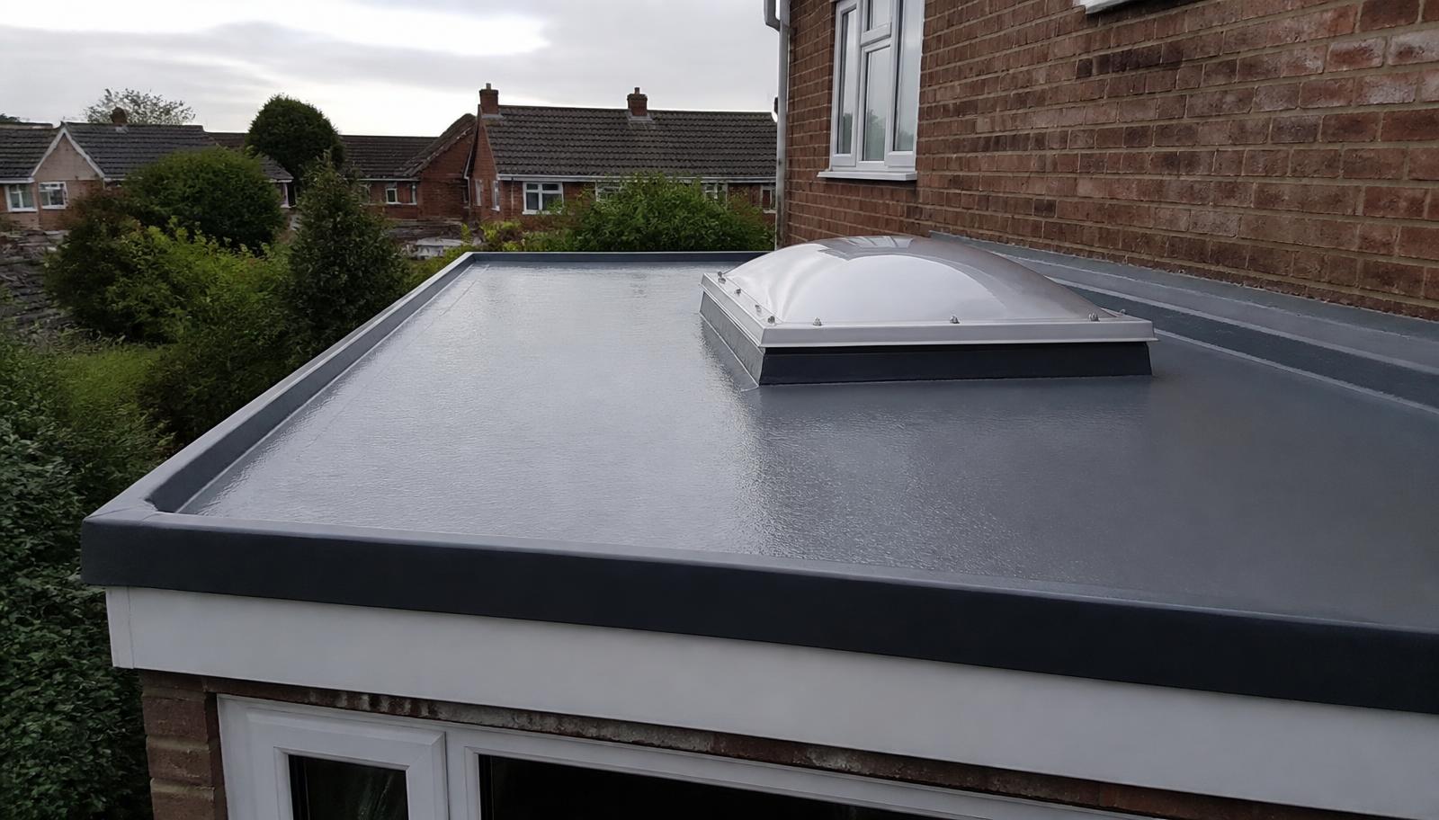 Mid-grey GRP fibreglass flat roof on a British extension with a domed rooflight and crisp drip trim against brickwork.